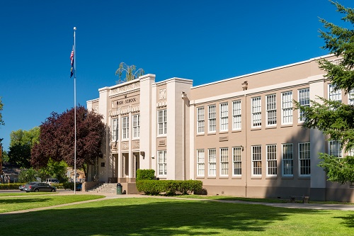 2-story square building with flat roof. More than a dozen windows line the walls of 1st and 2nd floors.