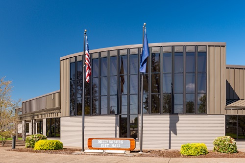 City Hall building completed in 1984 has tall windows floor to ceiling reaching 2 stories up. 2 flag poles in front.