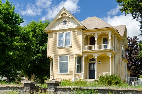 Two-story victorian style home. Porch on 1st and 2nd levels. Short stone wall in front of lawn surrounding walkway to house.