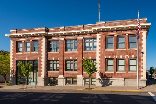 Brick 3-story building with sidewalk in front and a flag pole.