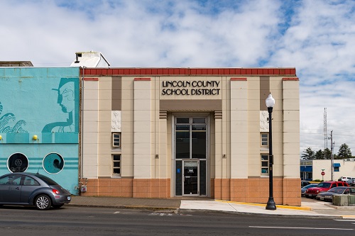 2-story brick building on the corner of Alder and SW Coast Hwy. Tall glass door with "Lincoln County School District" over top.