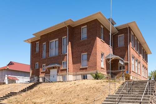 3-story builiding on a hill will stairs in center and right leading up to building.