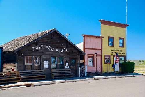 Single story log building with "This Ole House" printed on top. 2 buildings with false fronts like old time western towns. 