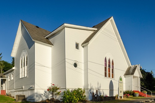 2-story church with sets of 3 stained glass windows on 2 sides of building. One round window in corner.