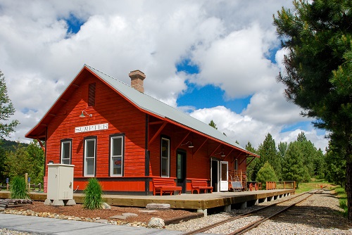 Single-story building with wood walking platform reaching to edge of train tracks.