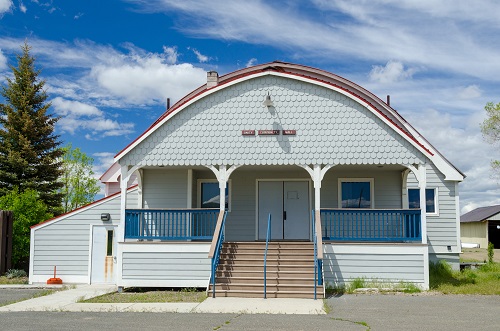 Single story house with elevated basement. A staircase leads to front double doors about 4 feet above street level. Rounded roof