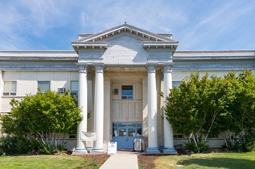 2-story school building with double doors. 2 columns on each side of front door hold up overhang.