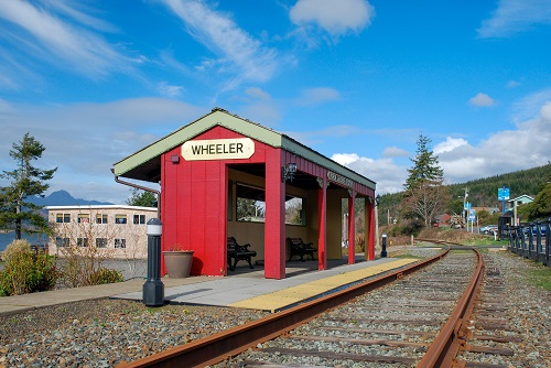 Benches under a covered waiting area next to train tracks. A sign on the covered waiting area says "Wheeler."